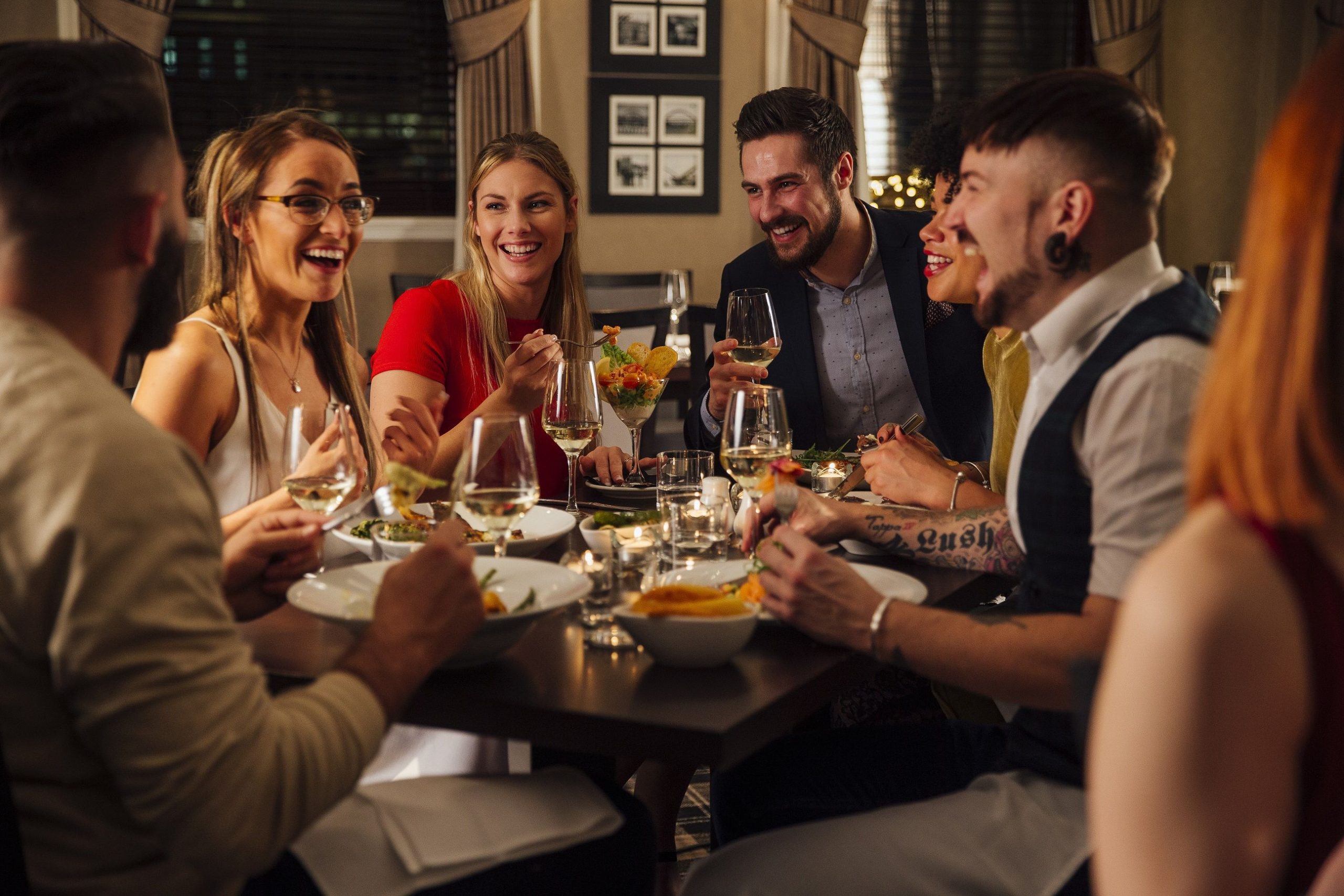 Group of friends are enjoying a meal together. They are talking and laughing while eating their starters and drinking champagne.